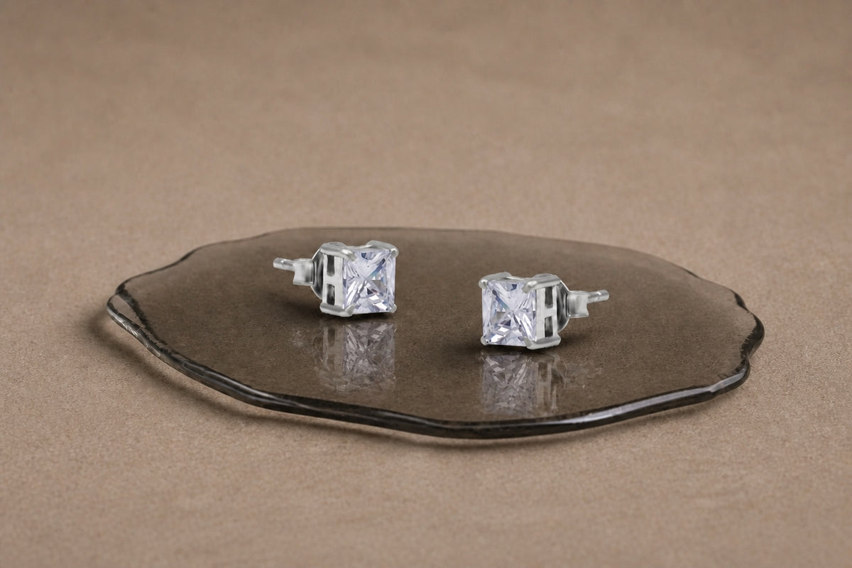 Sterling silver solitaire studs on a warm smoky glass display